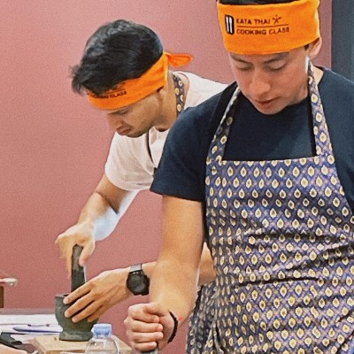 Two people in aprons and orange headbands using mortars and pestles in a cooking class.