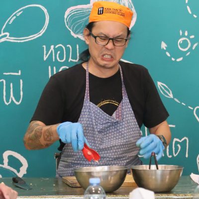 Person cooking, wearing apron and orange hat, in front of teal wall with text.