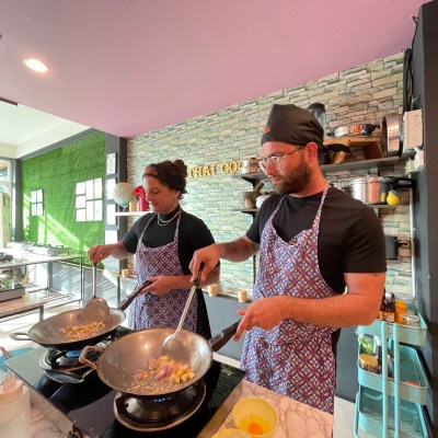 Two chefs cooking in a modern kitchen wearing aprons and hats.